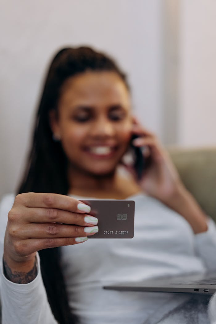 about-03 Focused shot of a woman holding a credit card, engaging in a phone conversation, depicting online shopping or banking.